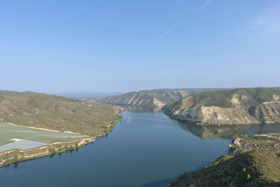 Scenic view of river by mountains against clear blue sky