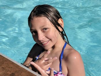 High angle portrait of smiling girl showing peace sign while swimming in pool