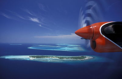 Cropped image of red airplane over blue sea against sky on sunny day