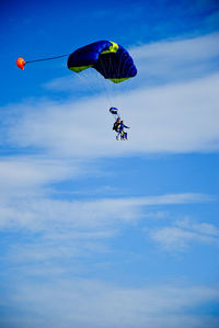 Low angle view of people paragliding against blue sky