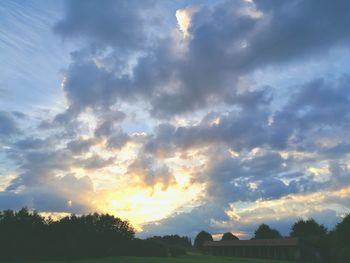 Silhouette of trees on field against cloudy sky