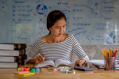 Woman studying with school supplies on table at home