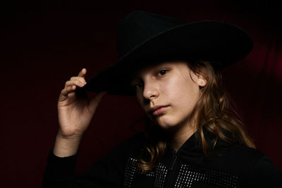 Portrait of young woman standing against black background