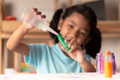 Cute girl pouring water in color bottle on table at home