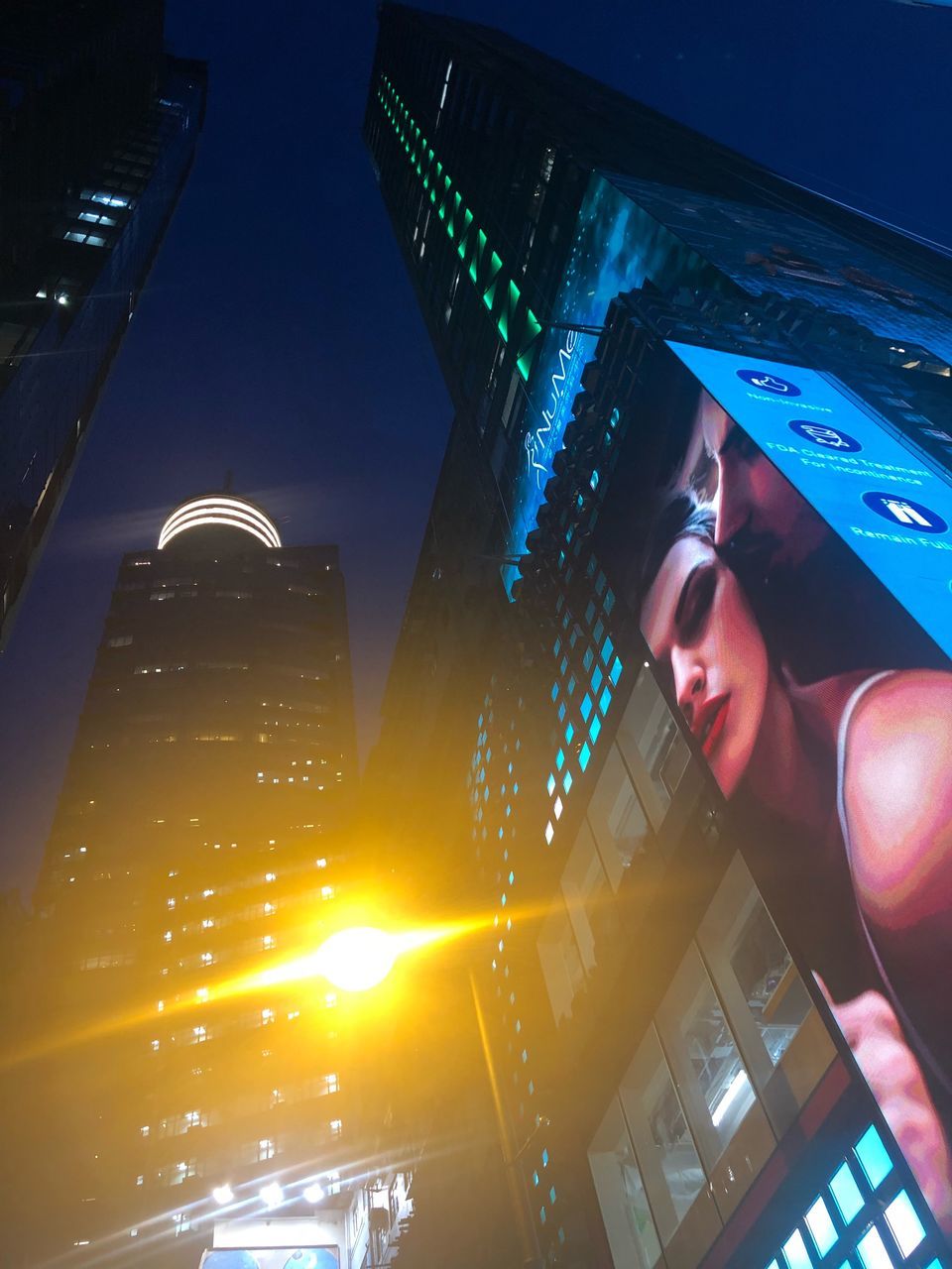 LOW ANGLE VIEW OF WOMAN ON ILLUMINATED BUILDING AGAINST SKY