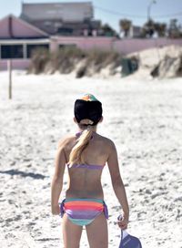 Rear view of girl in bikini playing matkot at beach on sunny day