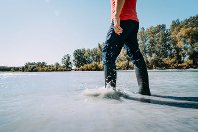 Low section of man standing on riverbank against clear sky