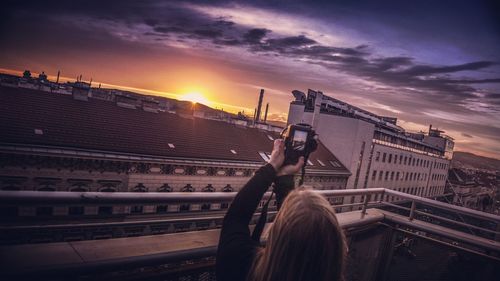 Rear view of woman photographing against sky during sunset