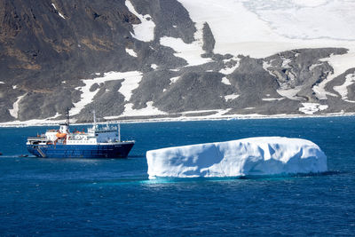 Research vessel in antarctica in front of a large iceberg on a sunny day