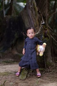 Portrait of cute girl with toy standing against tree