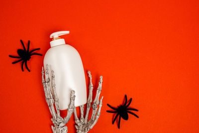 Cosmetic bottle with oil or soap on red halloween background with spiders and skeleton hands