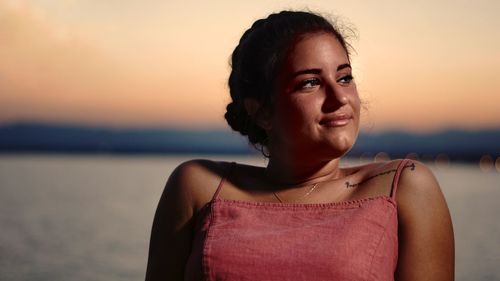 Portrait of beautiful woman standing against sea during sunset