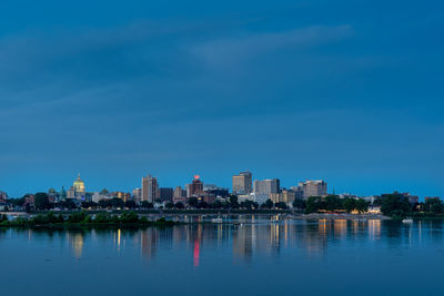 Buildings by river against blue sky