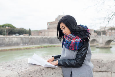 Side view of woman standing by retaining wall in city