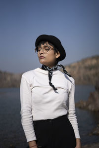 Young woman looking away while standing against sky