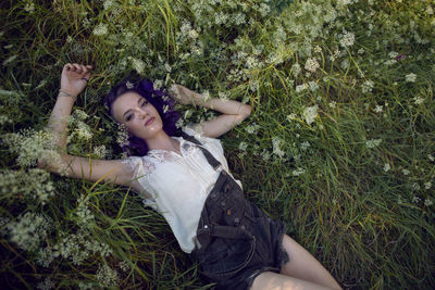 Portrait of a teenage girl with purple hair and an earring in her nose lie in the grass in nature