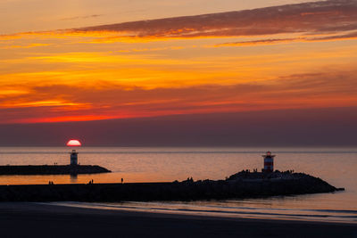 Lighthouse by sea against sky during sunset