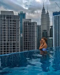 Full woman at infinity pool against modern building in city