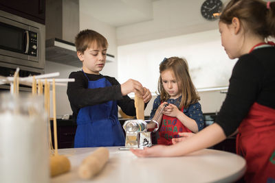 Family using pasta machine while preparing homemade noodles in home kitchen