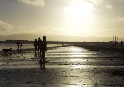 Silhouette people on beach against sky during sunset