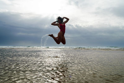 Woman jumping on beach against sky