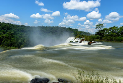 Scenic view of waterfall against blue sky during sunny day