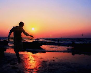 Silhouette man standing on beach against orange sky