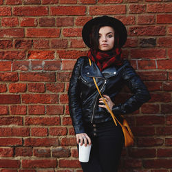 Portrait of young woman standing against brick wall