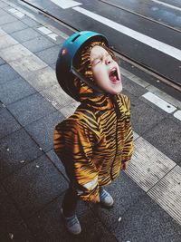 High angle view of boy in tiger print raincoat shouting on sidewalk