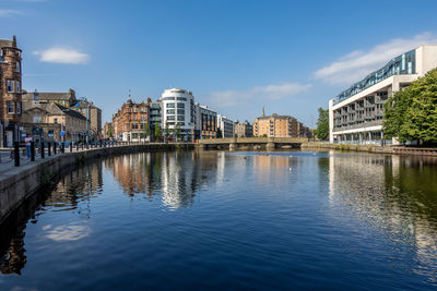 Bridge over river by buildings against sky in city