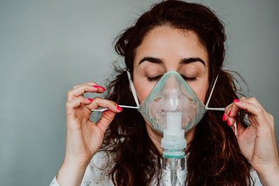 Close-up of woman wearing oxygen mask against gray background