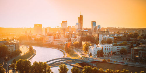 Bridge over river and buildings against sky during sunset