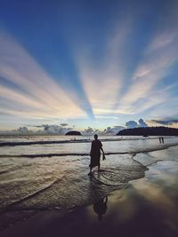 Rear view of woman standing at beach against sky during sunset