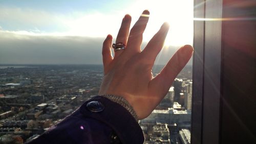 Cropped hand of woman touching glass window against cityscape