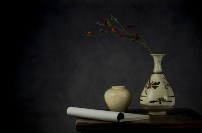 Still life of chinese antique porcelains with red chilies and old book on table against gray wall