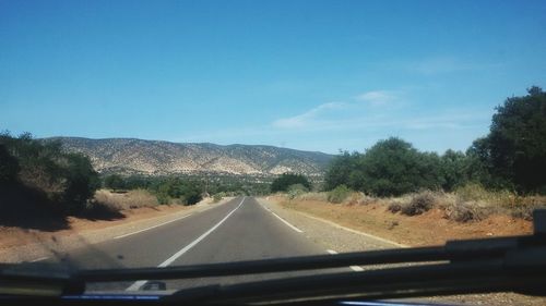 Road leading towards mountain against blue sky