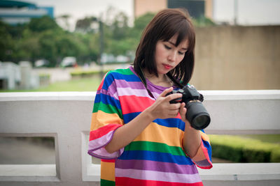 Young woman holding camera standing by railing