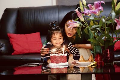 Smiling mother and boy blowing candles on cake at home