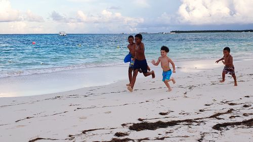 Kids running on beach against sky