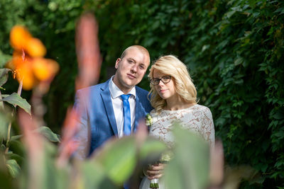 Portrait of bridal couple standing amidst plants at park