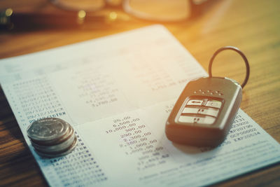 Close-up of bank book by car key and coins on table