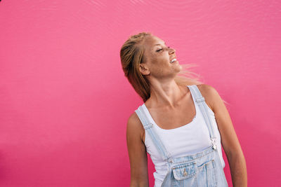 Woman shaking head while standing against pink wall