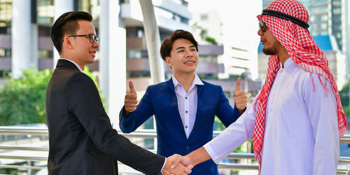 Businessmen shaking hands while standing with coworker standing in city