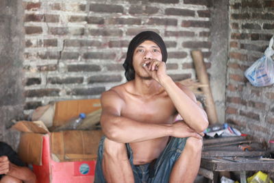 Full length of shirtless man sitting against wall