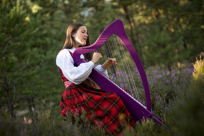 Woman singing and playing harp while sitting against trees