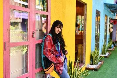 Portrait of smiling young woman leaning on closed door