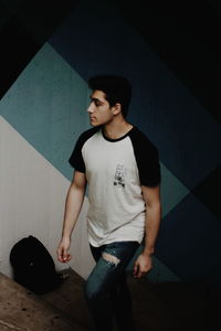 Young man looking away while standing against wall