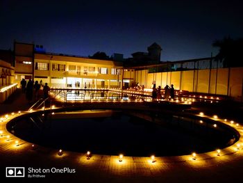 People at illuminated building against sky at night