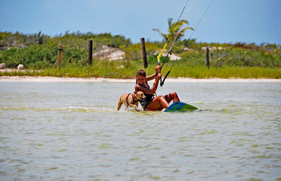 Woman kiteboarding in river with dogs running against sky