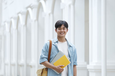 Portrait of young man standing with book outdoors